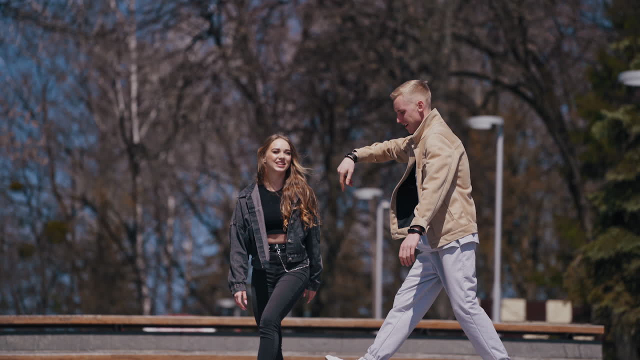 Happy young couple spend time outdoors. Beautiful girl enjoys the time with her positive boyfriend in the street. Teenagers having a date in the park.