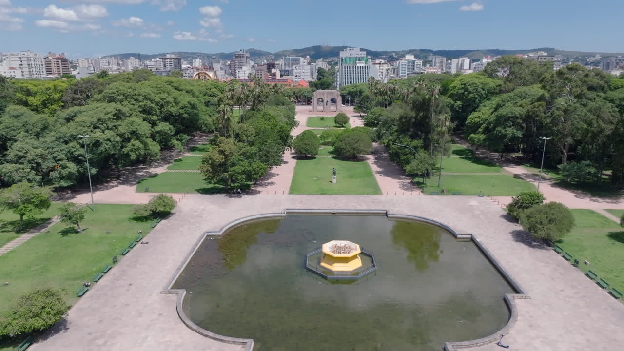 Vista aérea de drone sobre a fonte e o espelho d'água no Parque da Redenção em direção ao Monumento Expedicionário e ao Morro da Polícia em Porto Alegre, Brasil. Vídeos em 4K 10-bit