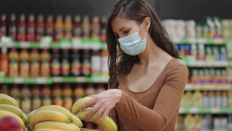 a woman in a mask in a supermarket chooses fruits and vegetables