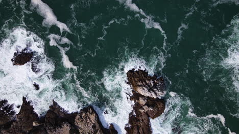 aerial - rough water leaving beautiful patterns along rocky coastline, top-down shot, flying horizontal