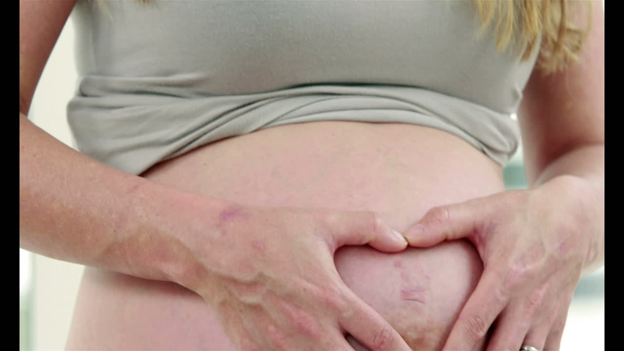 Donna incinta che fa un cuore con la mano sulla pancia.