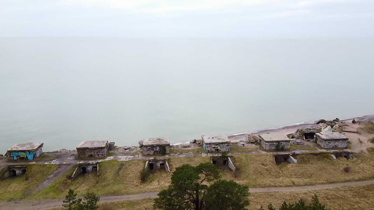 Aerial view of abandoned seaside fortification building at Karosta Northern Forts on the beach of Baltic sea in Liepaja in overcast spring day, pine wood, revealing drone shot moving backwards