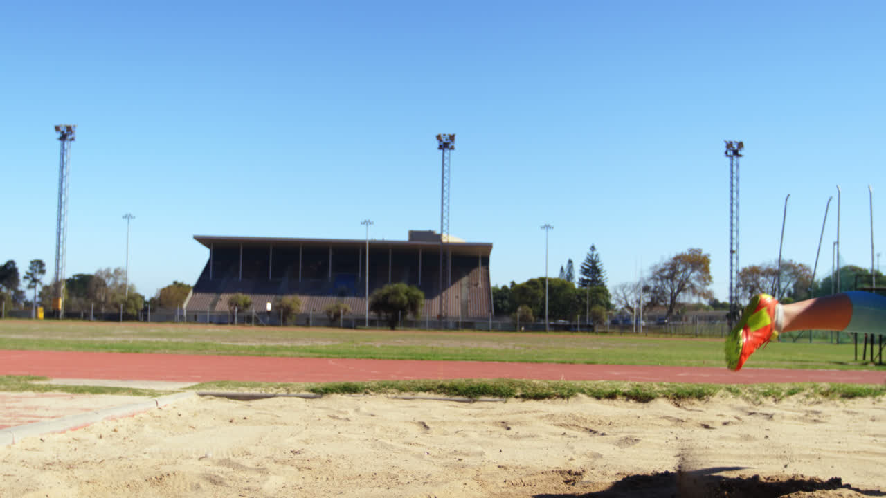 vista lateral de una atleta caucásica practicando salto de longitud en un recinto deportivo 4k