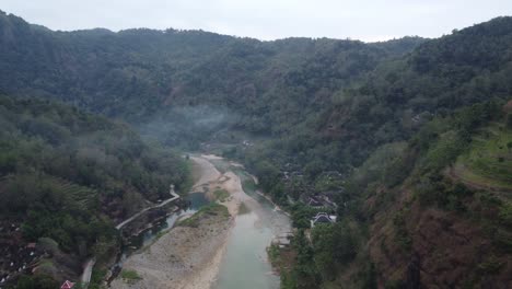 Beautiful-aerial-view-of-a-river-in-the-middle-of-the-mountains-in-the-morning-with-fog