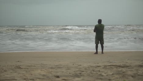 Mann-Mit-Dem-Rücken-Am-Ufer-Eines-Strandes,-Der-Mit-Einer-Leine-Fischt