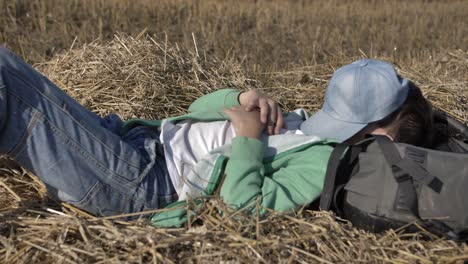 tired boy sleeping in the hay outdoors, resting his head on a backpack