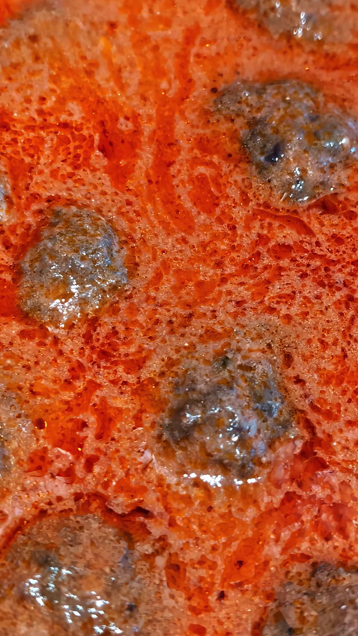 Polpette che sobbollono e ribollono delicatamente in una ricca salsa di pomodoro rossa e corposa, creando una scena di cucina calda e appetitosa. Video verticale, ideale per i social media