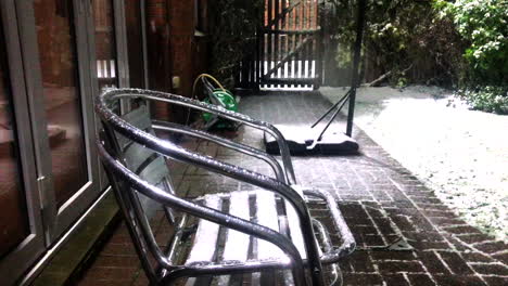 nieve cayendo sobre sillas de metal apiladas en el jardín trasero con puerta con sillas en el centro de la toma