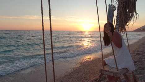 young girl on swing next to beautiful ocean at sunset