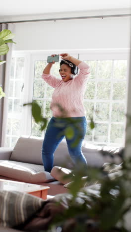 vertical video of happy african american woman dancing and listening music on headphones at home