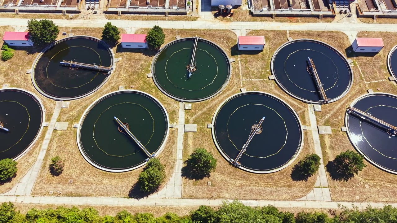 Water treatment facility shows multiple circular tanks used for purification at a large site surrounded by trees during daylight