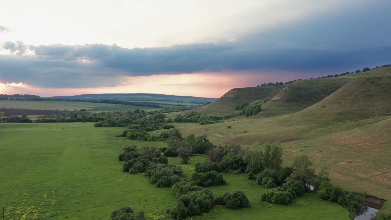 vista del hermoso terreno donde crece la hierba verde. altas montañas contra el cielo nublado. cielo en los rayos rosados de la puesta de sol.