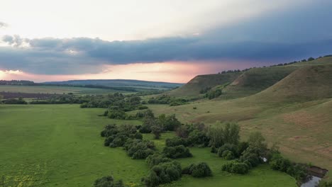 view of the beautiful terrain where the green grass grows. high mountains against the cloudy sky. sky in the pink rays of the sunset.