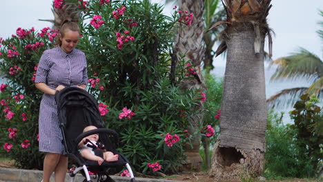 during the summer in a park adorned with blossoms, a young mother takes a leisurely walk with her baby in a stroller. she exudes joy while accompanying her son