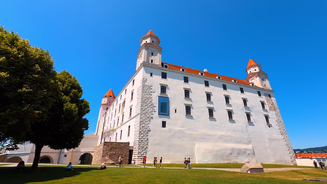 Tourists walk around the walls of the beautiful Bratislava Castle. Low angle view at the famous Slovak landmark on sunny day
