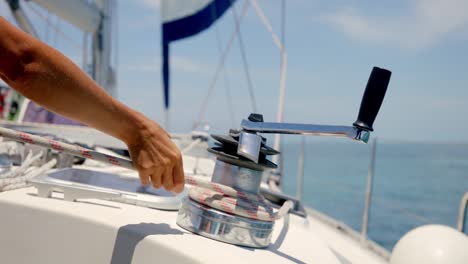 Close-Up-of-Sailman-Hands-Unwinding-Rope-From-Winch-of-Sailboat-on-Sunny-Tropic-Day,-Slow-Motion-Full-Frame