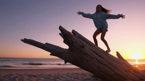girl balancing on driftwood at sunset