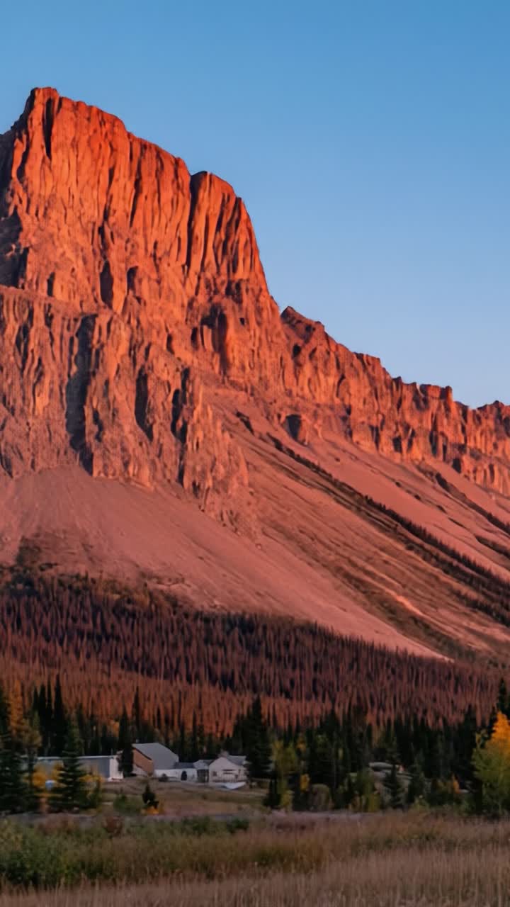 Maestoso paesaggio montano al tramonto: una vista mozzafiato di cime aspre circondate da una foresta lussureggiante e una pittoresca fattoria in primo piano.