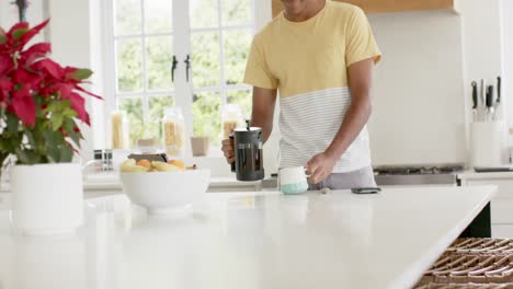 hombre biracial feliz haciendo café en una cocina brillante, cámara lenta