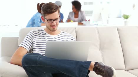 Handsome-designer-sitting-on-couch-working-on-laptop