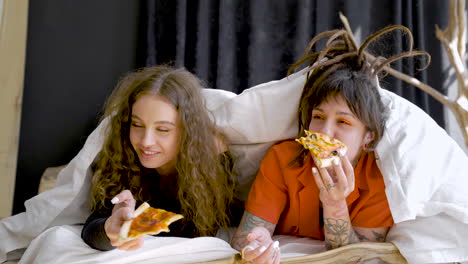 Young-Girl-Friends-Laying-On-Bed-While-Talk-And-Eat-Pizza