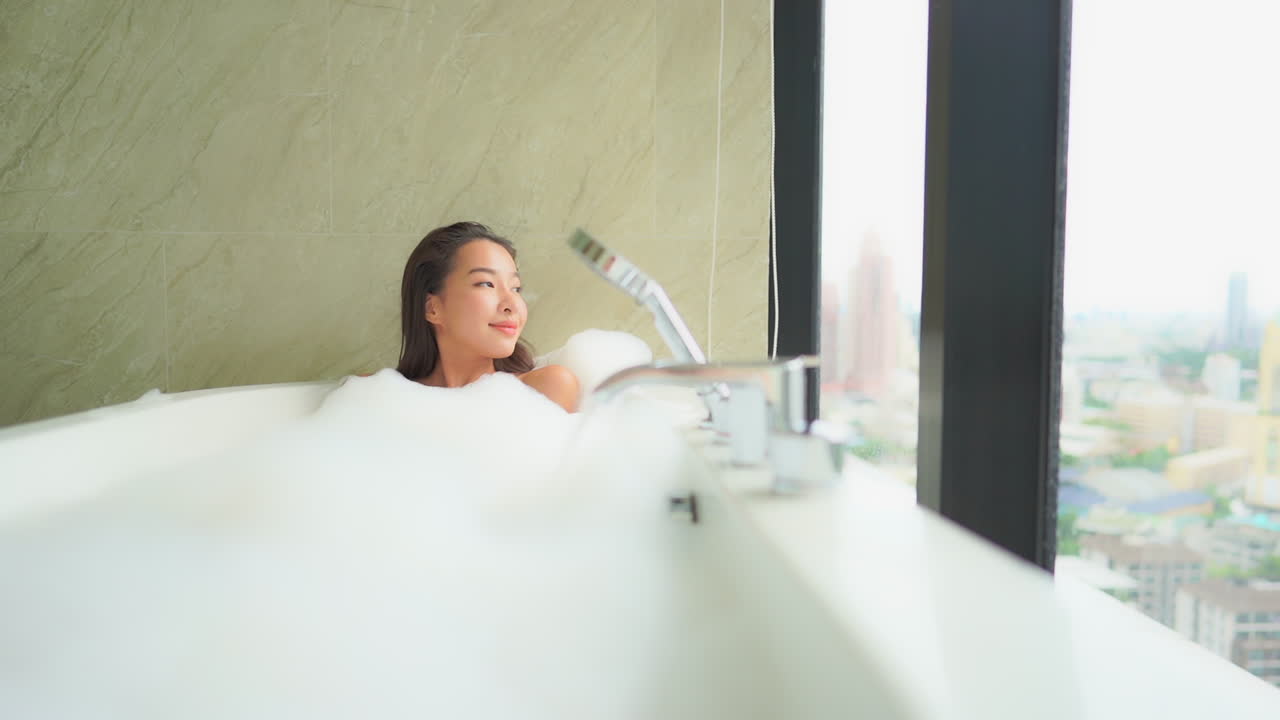 A beautiful young woman enjoys a spa tube and bubble bath while looking out at an urban skyline, Bangkok, Thailand