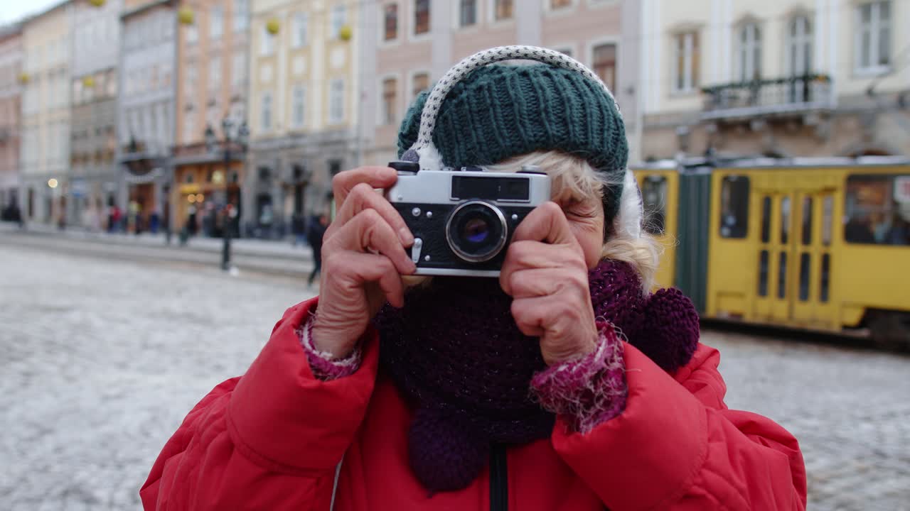 turista anciana tomando fotos con una cámara fotográfica, usando un dispositivo retro en el centro de la ciudad de invierno