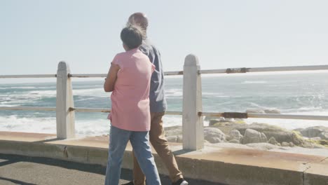 Happy-senior-african-american-couple-walking-along-promenade-by-the-sea,-slow-motion