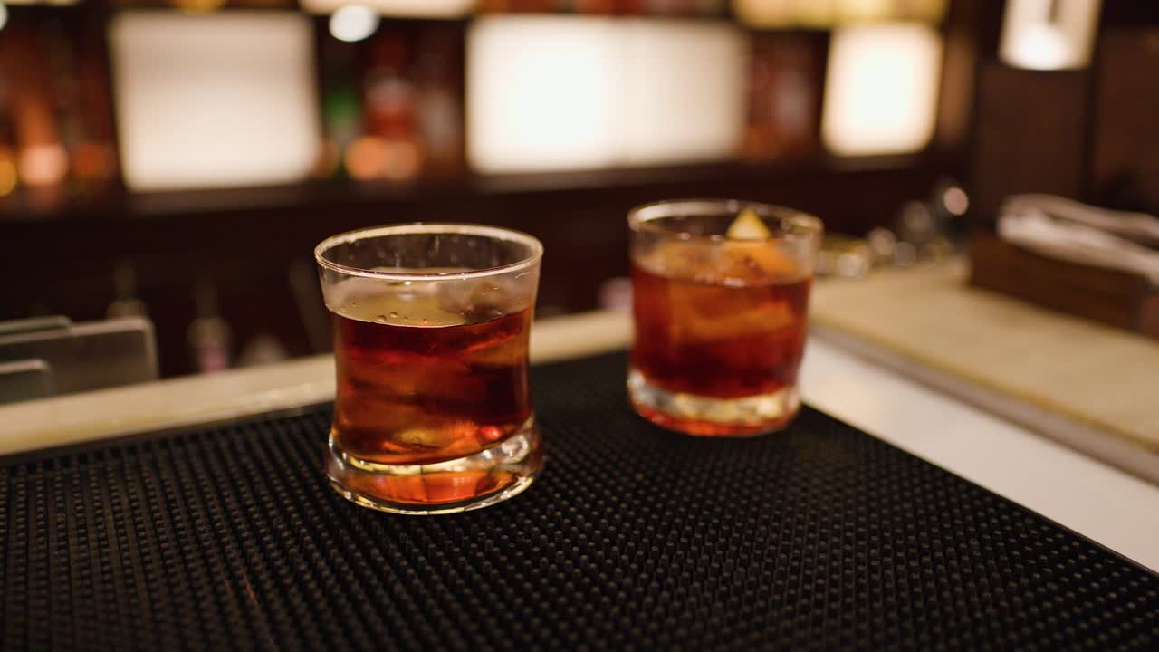 Bartender stirs whiskey cocktails in low light bar, warm ambient lighting, close-up perspective