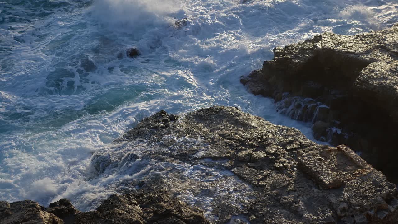 tomada de arriba hacia abajo panorámica a la derecha de las olas azules del océano golpeando las rocas durante la hora dorada y el amanecer en siracusa, sicilia (sicilia, italia)