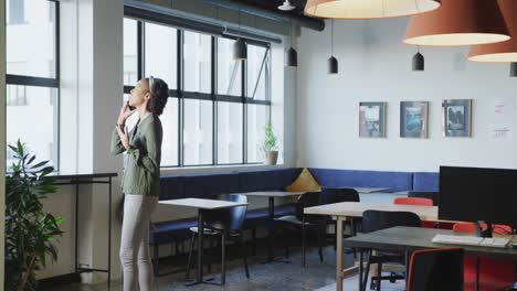 mujer de negocios afroamericana en la ventana usando un teléfono inteligente sola en la oficina