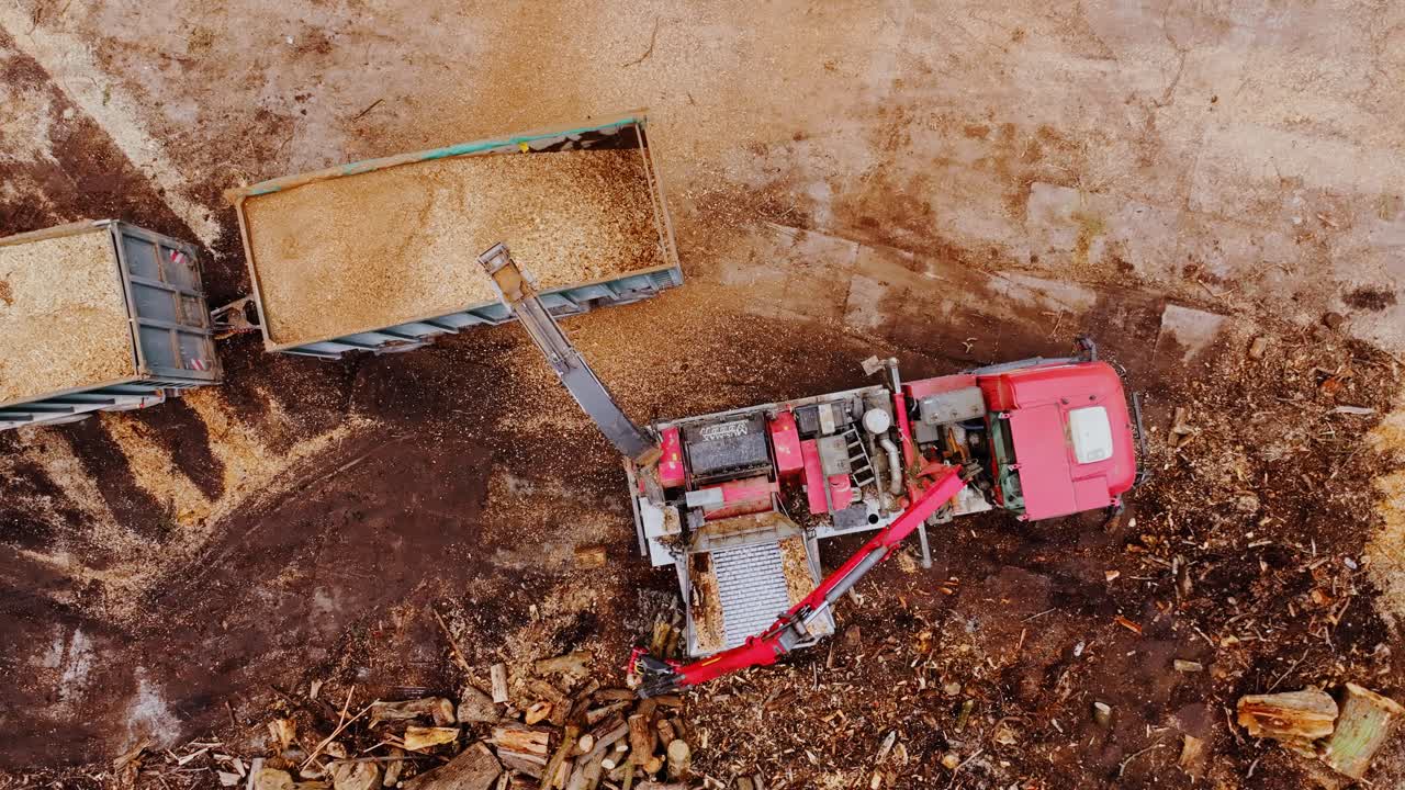 Drone slowly ascends, rotates, capturing top-down view of wood chipping process