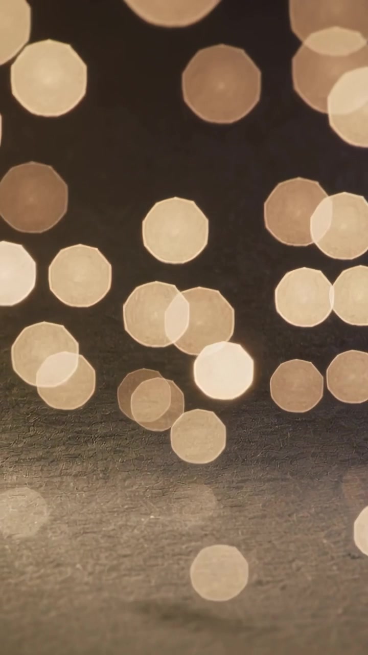 Vertical video: Shifting soft warm bokeh across dim room after slight focus shift over dark texture