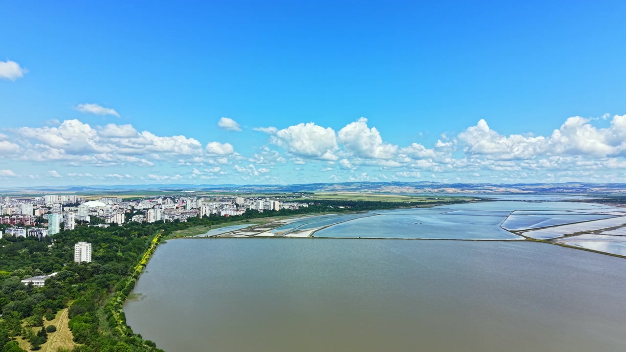 昼間のブルガス市街の眺め：手前に建物と水、背景に雲のある澄んだ空