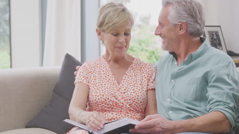 Senior-Retired-Couple-Sitting-On-Sofa-At-Home-Enjoying-Looking-Through-Family-Photo-Album