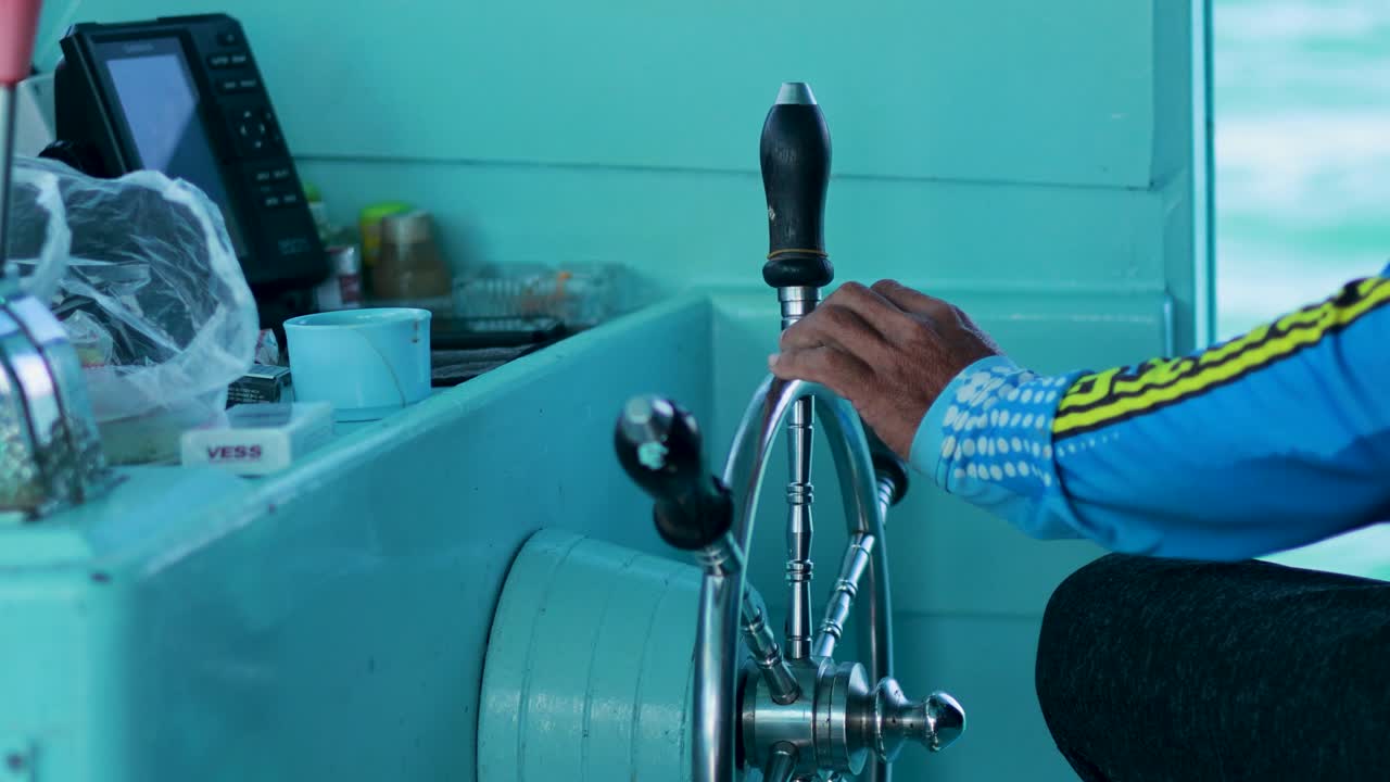 A captain skillfully steers a fishing boat using a helm wheel in Phuket, Thailand. Bright lighting highlights the vibrant marine setting