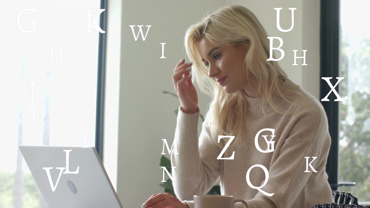 Donna che digita al laptop, lettere fluttuano sullo schermo, poi si ferma e osserva, riflettendo su un lavoro tecnologico.