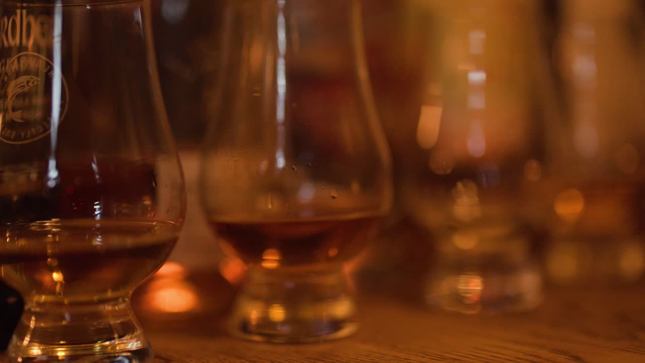 Una mano sfocata prende un bicchiere Glencairn di whisky ambrato in un pub accogliente