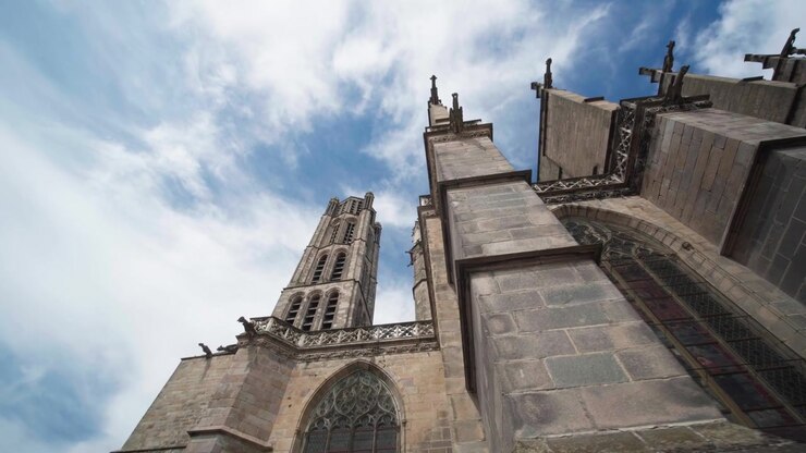 Architettura della Cattedrale di Limoges con torri in pietra, archi rampanti e gargoyle contro un cielo nuvoloso. Prospettiva dal basso.
