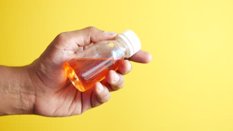 close-up of a hand holding a small bottle of orange medicine