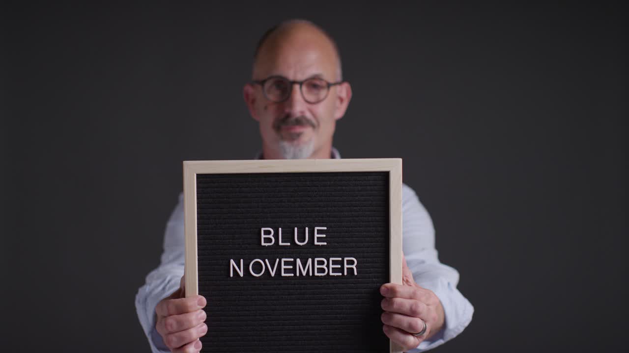 Studio Portrait Of Mature Man Holding Up Sign Reading Blue November Promoting Awareness Of Men's Health And Cancer