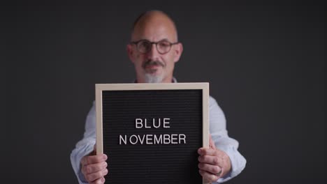 Studio Portrait Of Mature Man Holding Up Sign Reading Blue November Promoting Awareness Of Men&#039;s Health And Cancer