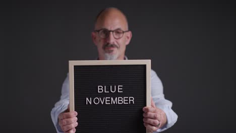 studio portrait of mature man holding up sign reading blue november promoting awareness of men's health and cancer