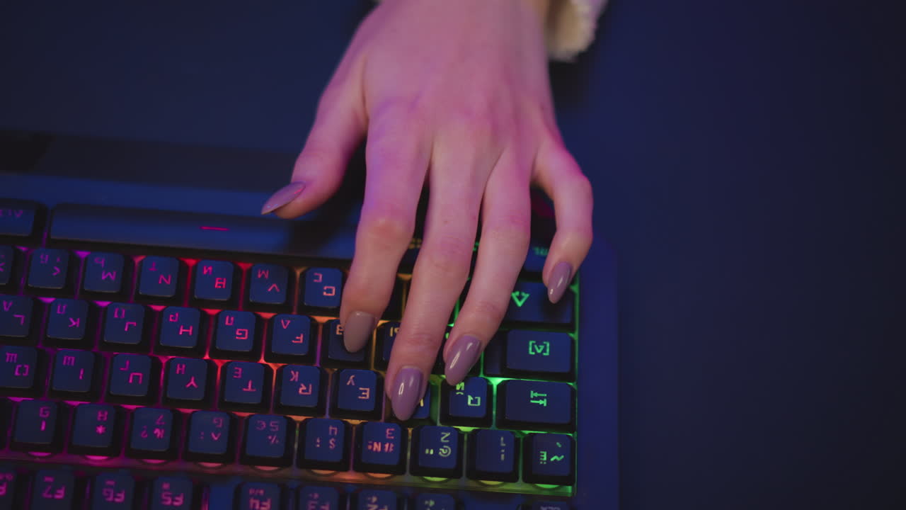 top down view of girl hand in fluffy sweater with long polished nails typing on rgb mechanical keyboard glowing with vibrant colors in dark room, showing focus on gaming or computer work