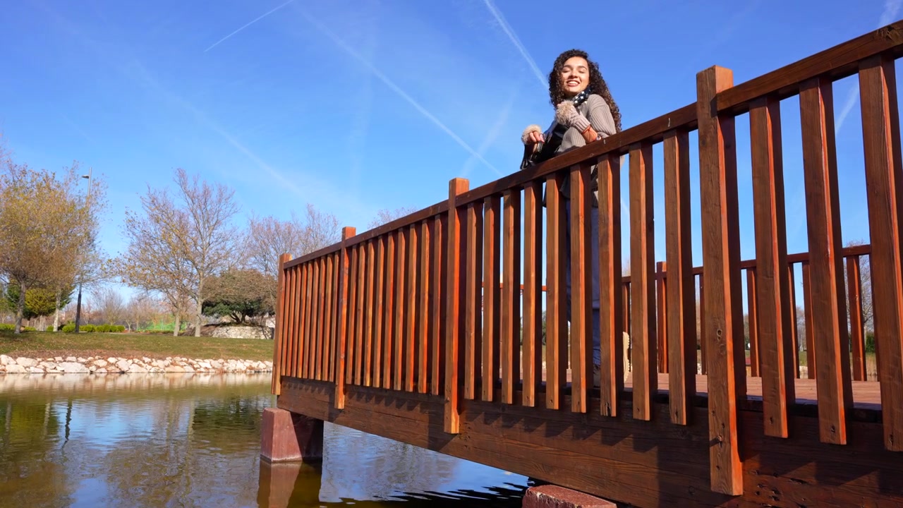 Allegra donna riccia che canta e suona l'ukulele su un molo di legno su un lago di un parco