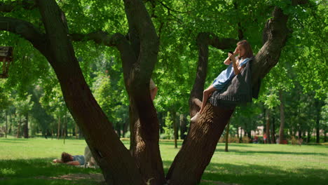 Fröhliche-Kinder-Sitzen-Auf-Einem-Baum-Beim-Picknick.-Süße-Geschwister-Spielen-Auf-Breiten-Ästen.