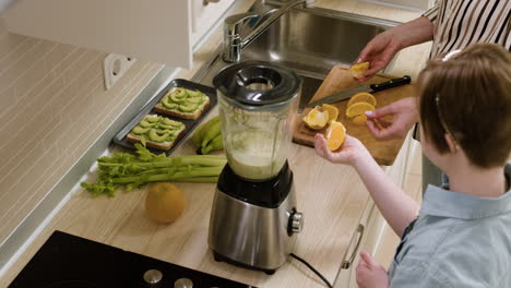 mother and her daughter cutting fruits and putting inside a blender to do smoothie