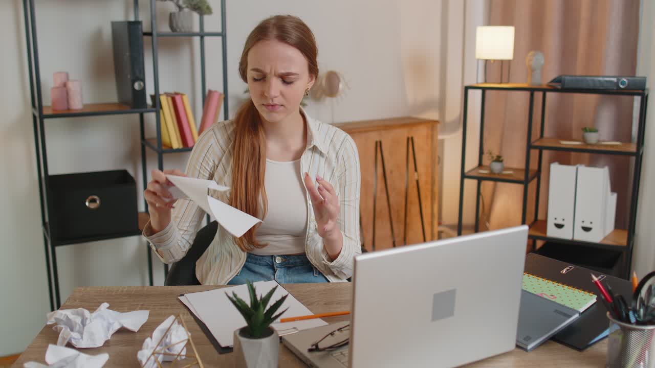mujer joven triste trabajando en la oficina de casa se desmorona tirando hojas de papel con malas ideas y errores