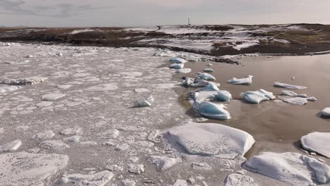 drone captures floating icebergs in the frozen fjallsárlón glacial lake, with snowy hills and a winding road in the distance, near vatnajökull in iceland.