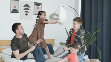 playful young family having fun with children they are fighting pillows in the bedroom playful young family having fun with children they are fighting pillows in the bedroom happy family relaxes playing at home on the bed